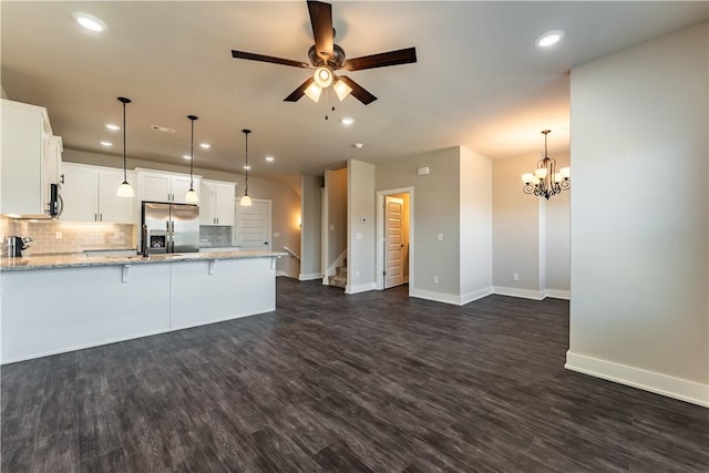 kitchen with dark wood-type flooring, light stone counters, stainless steel fridge with ice dispenser, hanging light fixtures, and white cabinets