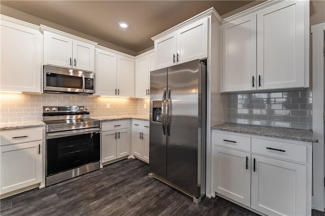 kitchen featuring dark wood-type flooring, white cabinets, stainless steel appliances, light stone countertops, and backsplash