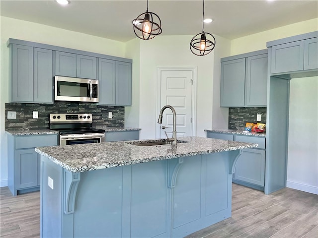 kitchen with decorative light fixtures, backsplash, stainless steel appliances, sink, and light stone counters