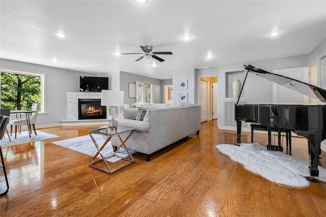 living room featuring ceiling fan, a stone fireplace, and light wood-type flooring