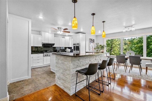 kitchen with hanging light fixtures, white cabinets, a kitchen bar, decorative backsplash, and tile patterned floors