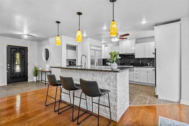 kitchen featuring white cabinetry, built in refrigerator, a breakfast bar, and a kitchen island with sink