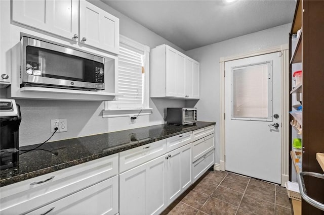 kitchen featuring dark tile patterned floors, dark stone countertops, and white cabinets