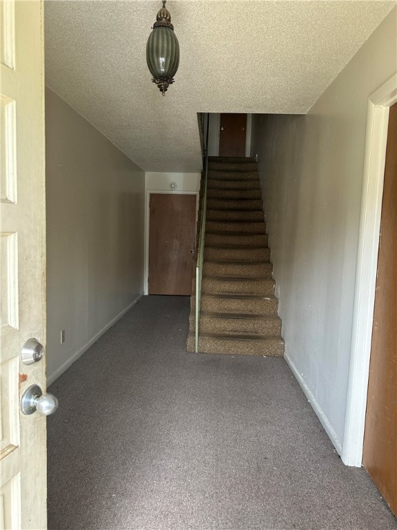 staircase featuring a textured ceiling and dark carpet