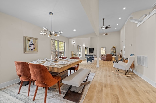 dining area featuring light wood-type flooring, ceiling fan with notable chandelier, and a high ceiling