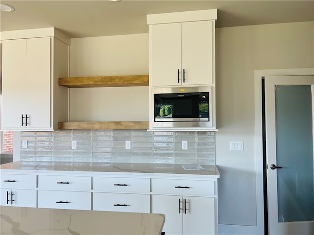 kitchen with stainless steel microwave, white cabinets, and tasteful backsplash