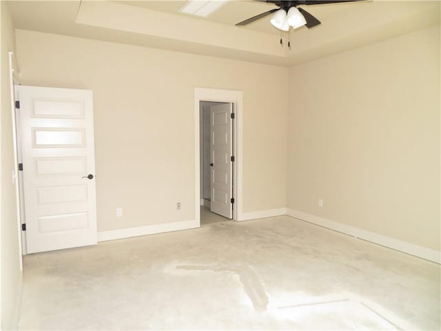 spare room with concrete flooring, a tray ceiling, a ceiling fan, and baseboards