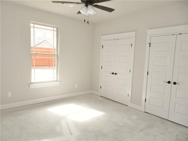 unfurnished bedroom with concrete flooring, a ceiling fan, baseboards, and two closets