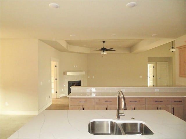 kitchen with light stone counters, open floor plan, a tray ceiling, a fireplace, and a sink