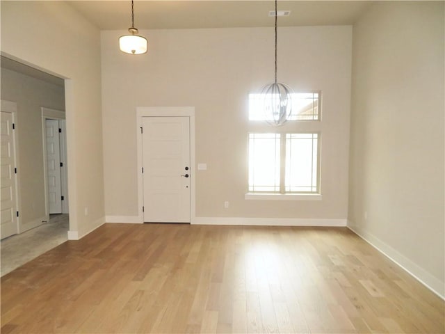 entrance foyer with visible vents, baseboards, a towering ceiling, light wood-style floors, and a notable chandelier