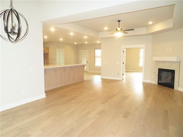 unfurnished living room with light wood-type flooring, a tray ceiling, a wealth of natural light, and a high end fireplace