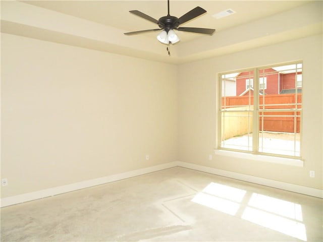 spare room featuring concrete flooring, a ceiling fan, visible vents, baseboards, and a tray ceiling