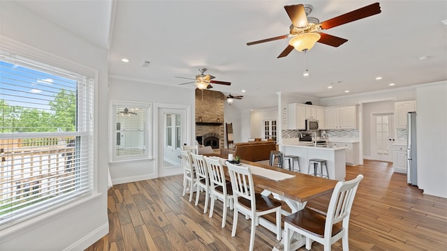 dining area featuring a stone fireplace, ornamental molding, and light wood-type flooring