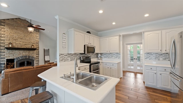 kitchen with hardwood / wood-style flooring, white cabinetry, backsplash, stainless steel appliances, and a stone fireplace