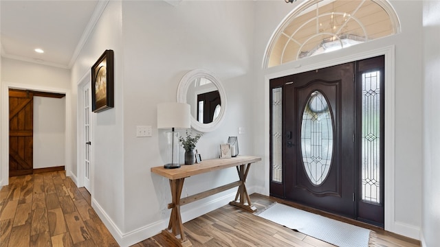 entrance foyer featuring hardwood / wood-style flooring, a healthy amount of sunlight, ornamental molding, and a barn door