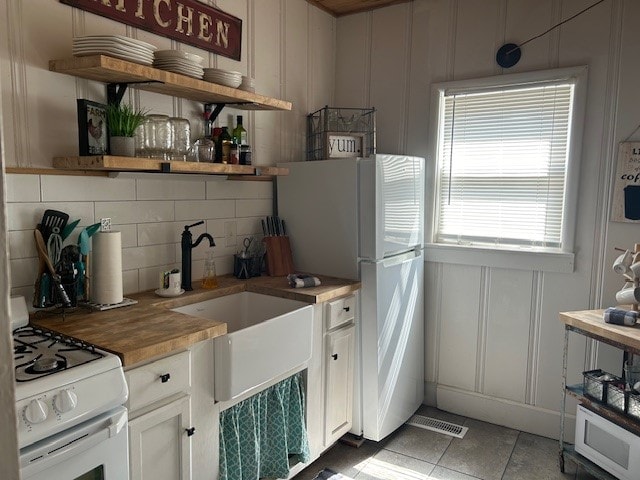 kitchen with light tile flooring, tasteful backsplash, butcher block counters, white cabinets, and white appliances