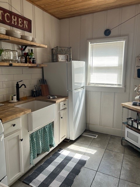 kitchen with tasteful backsplash, wooden counters, wood ceiling, tile floors, and white cabinetry