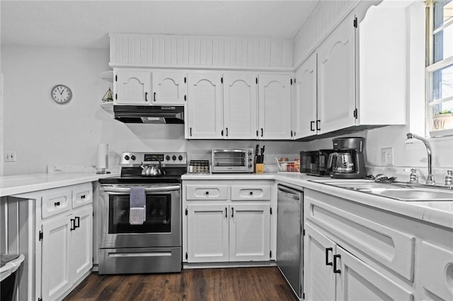 kitchen featuring dark wood finished floors, stainless steel appliances, white cabinetry, a sink, and ventilation hood