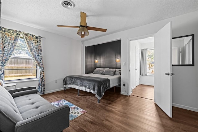 bedroom featuring a textured ceiling, ceiling fan, wood finished floors, visible vents, and baseboards