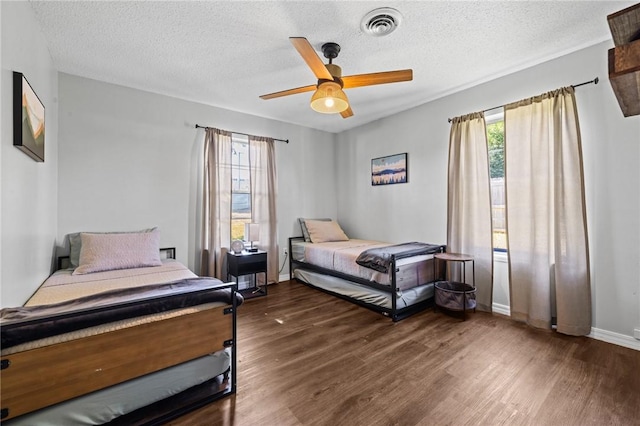 bedroom featuring visible vents, a ceiling fan, a textured ceiling, wood finished floors, and baseboards