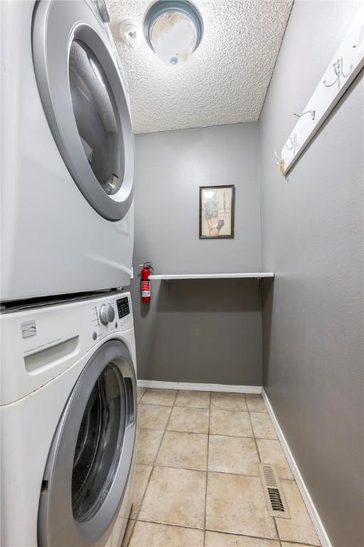 clothes washing area with laundry area, light tile patterned floors, visible vents, a textured ceiling, and stacked washing maching and dryer