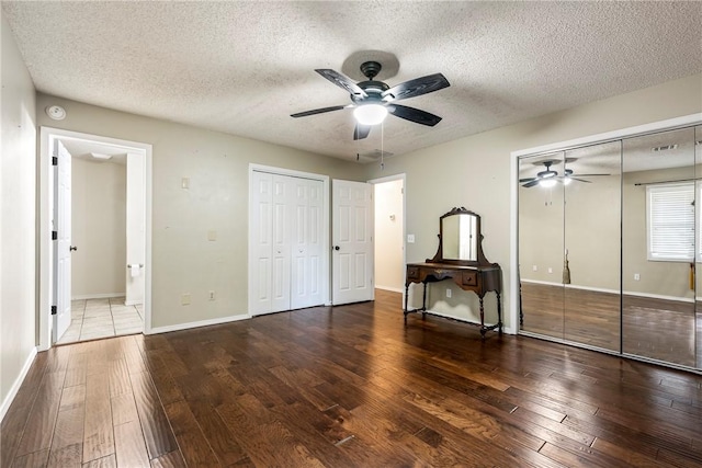 unfurnished bedroom with a textured ceiling, wood-type flooring, baseboards, and multiple closets