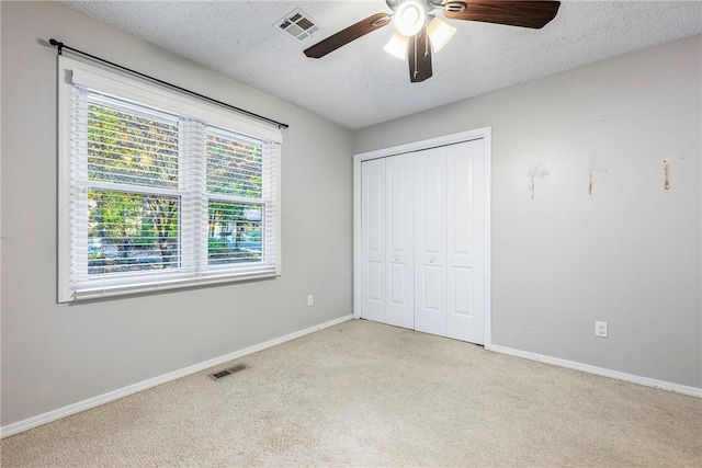 unfurnished bedroom featuring a textured ceiling, baseboards, visible vents, and light colored carpet