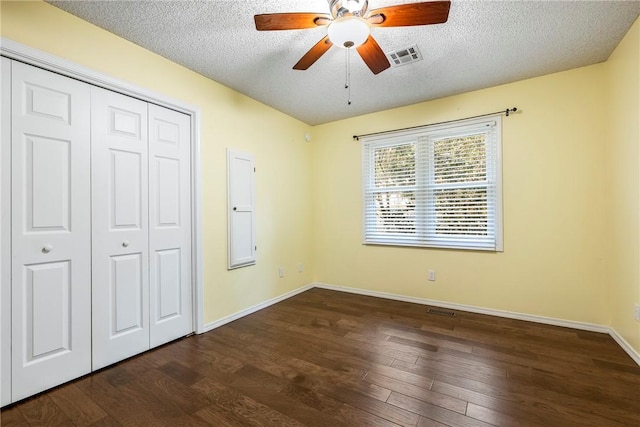 unfurnished bedroom featuring dark wood-style floors, a closet, a textured ceiling, and baseboards