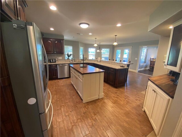 kitchen featuring stainless steel appliances, an island with sink, dark brown cabinets, and kitchen peninsula