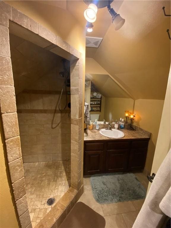 bathroom with lofted ceiling, vanity, tile patterned flooring, and a tile shower