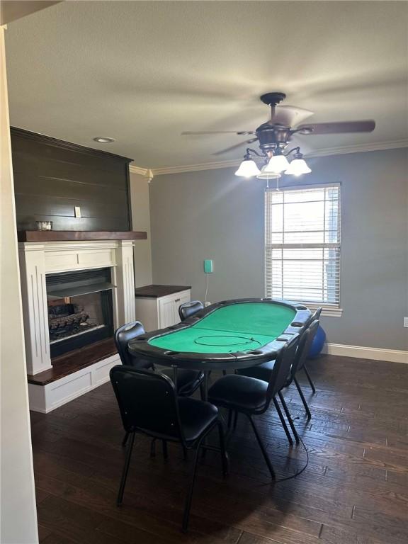 recreation room with crown molding, dark hardwood / wood-style floors, ceiling fan, and a fireplace