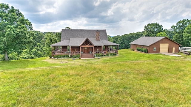 view of front facade featuring a detached garage, a porch, a front lawn, an outdoor structure, and a forest view