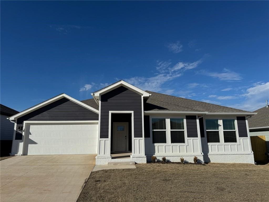 view of front of house with a garage, concrete driveway, a front lawn, and a shingled roof