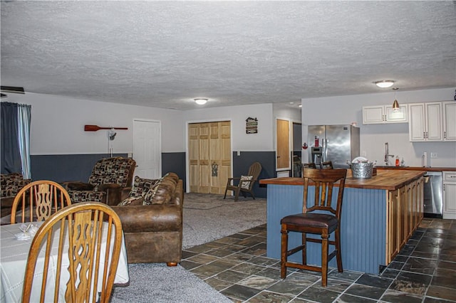 kitchen featuring wooden counters, a kitchen bar, dark carpet, stainless steel appliances, and white cabinetry