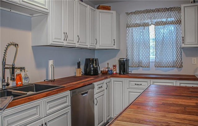 kitchen featuring butcher block countertops, stainless steel dishwasher, white cabinetry, and sink