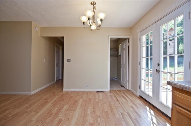 spare room featuring a textured ceiling, a chandelier, light hardwood / wood-style flooring, and french doors