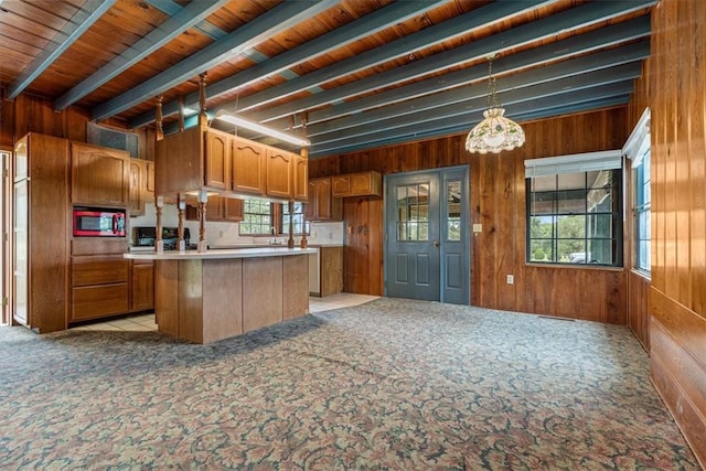 kitchen featuring wood walls, stainless steel microwave, brown cabinets, and light colored carpet