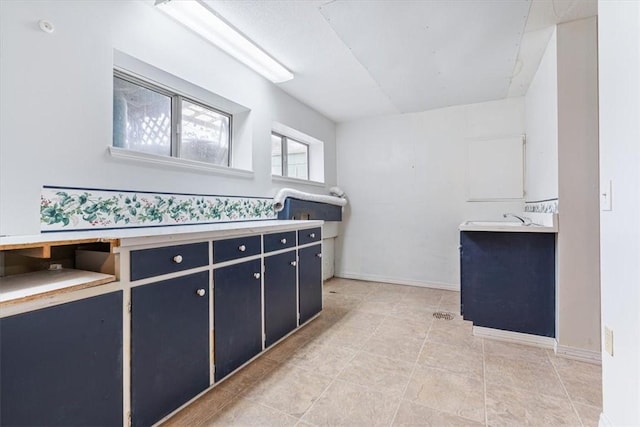 kitchen featuring blue cabinetry, a sink, and baseboards