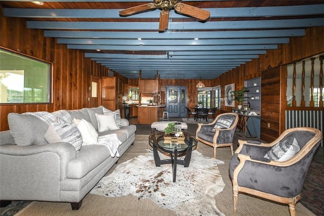 living area with beamed ceiling, wood walls, and a ceiling fan