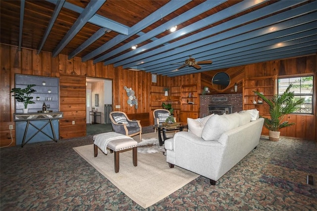 carpeted living area with ceiling fan, wooden walls, a fireplace, and beam ceiling