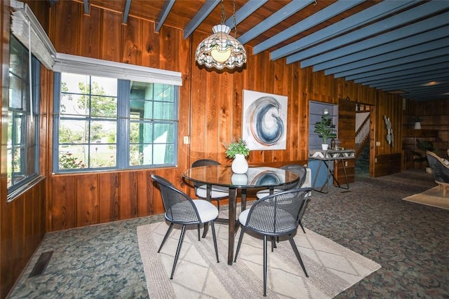 carpeted dining area featuring beamed ceiling, visible vents, and wooden walls