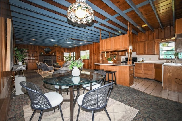 dining area featuring light tile patterned floors, a glass covered fireplace, wood walls, wooden ceiling, and beamed ceiling