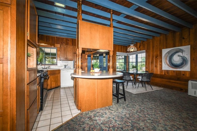 kitchen featuring light tile patterned floors, wooden walls, brown cabinetry, white dishwasher, and black gas stove