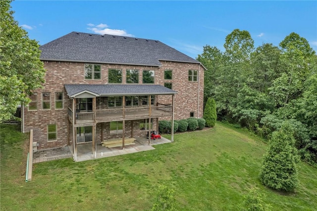 back of house with a shingled roof, a patio area, a lawn, and brick siding