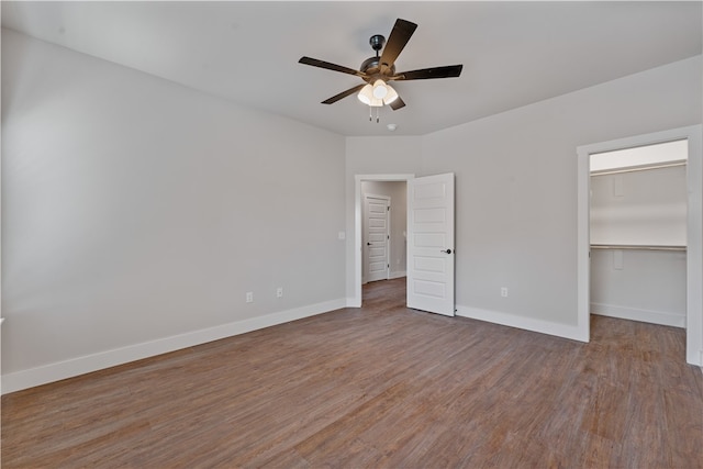 unfurnished bedroom with a spacious closet, a closet, hardwood / wood-style flooring, and ceiling fan