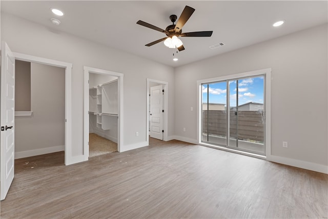 unfurnished bedroom with access to outside, a closet, a spacious closet, light wood-type flooring, and ceiling fan