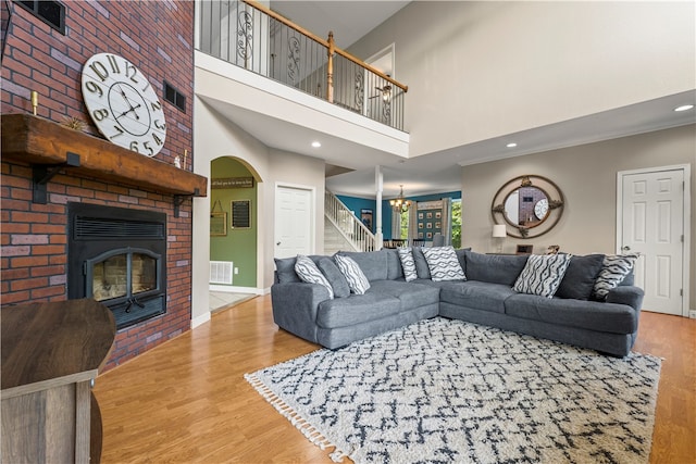 living room with hardwood / wood-style floors, a notable chandelier, a high ceiling, and a brick fireplace