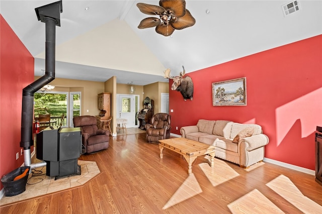 living room featuring ceiling fan, hardwood / wood-style floors, beam ceiling, a wood stove, and high vaulted ceiling