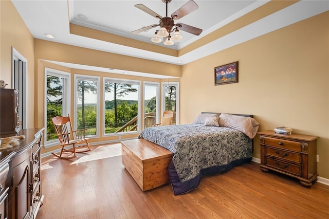 bedroom with a tray ceiling, ornamental molding, ceiling fan, and hardwood / wood-style floors