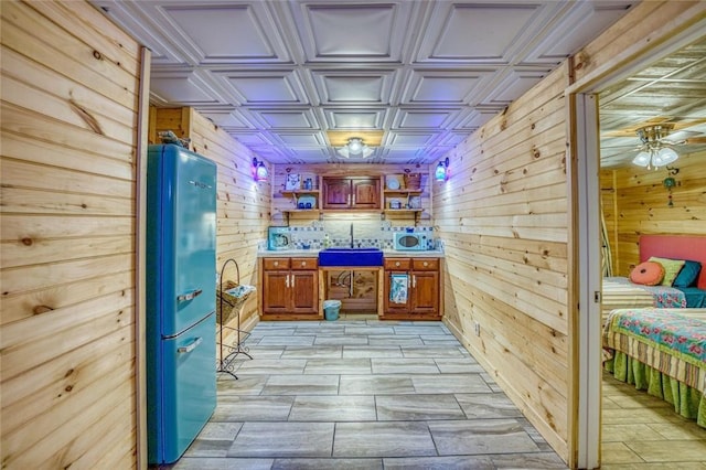 bar featuring wooden walls, ceiling fan, sink, and stainless steel refrigerator